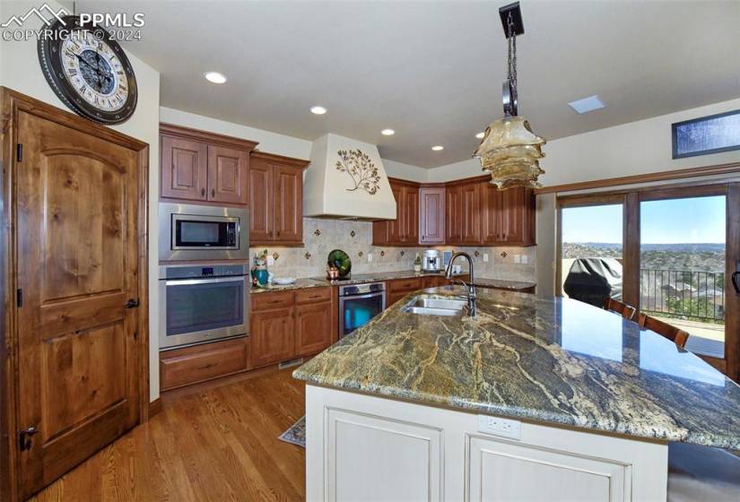 Kitchen with sink, an island with sink, custom range hood, and stainless steel appliances