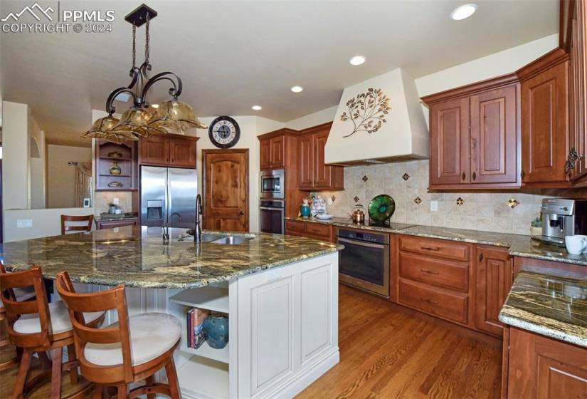 Kitchen featuring stainless steel appliances, dark stone counters, a chandelier, custom range hood, and tasteful backsplash