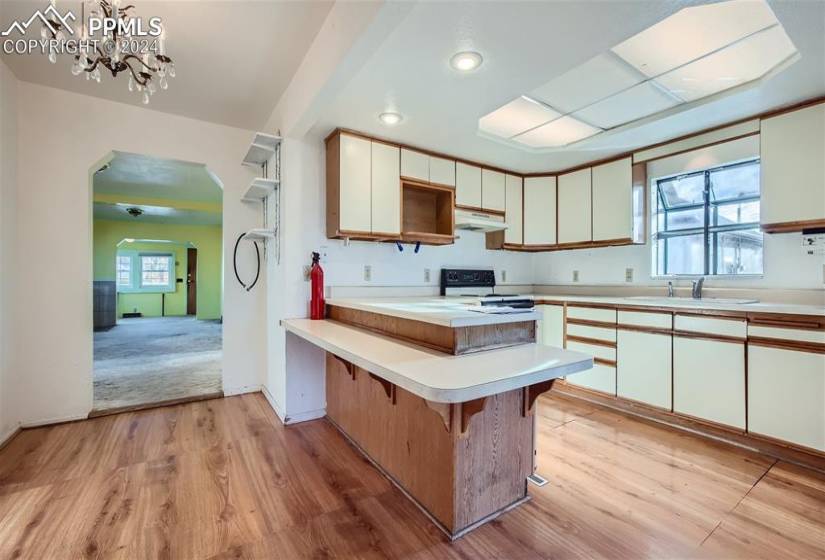 Kitchen with electric range, light hardwood / wood-style flooring, a breakfast bar, and a chandelier