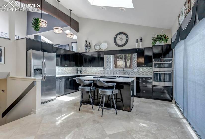 Kitchen with appliances with stainless steel finishes, hanging light fixtures, tasteful backsplash, a kitchen island, and light tile floors