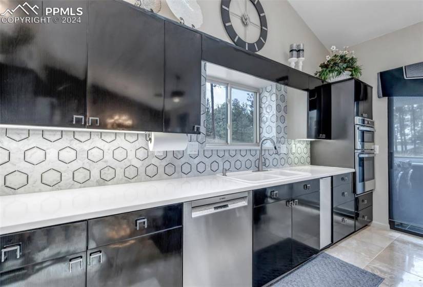 Kitchen with appliances with stainless steel finishes, backsplash, vaulted ceiling, light tile floors, and sink