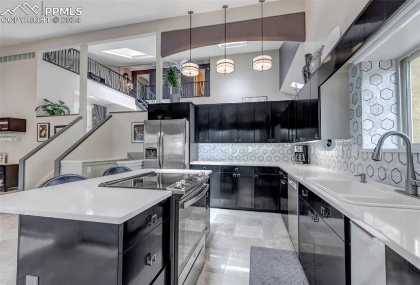 Kitchen featuring stainless steel appliances, backsplash, sink, pendant lighting, and light tile flooring