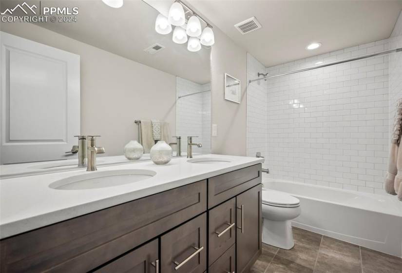 Full bathroom with tile floors, dual vanity, toilet, and tiled shower / bath combo