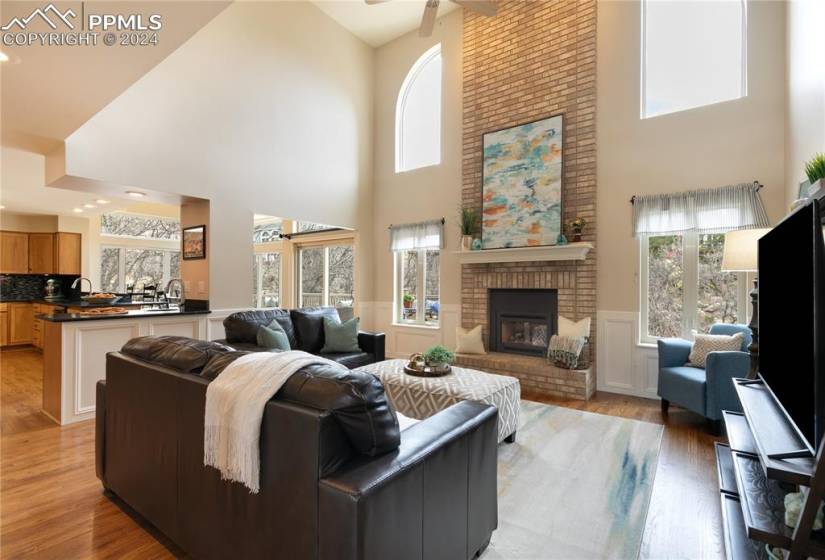 Main level family room featuring brick fireplace, ceiling fan, light hardwood floors,  and high vaulted ceiling and lots of light