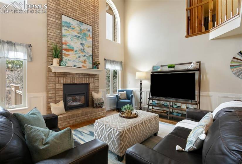 Living room featuring brick wall, hardwood / wood-style floors, a brick fireplace, and a towering ceiling