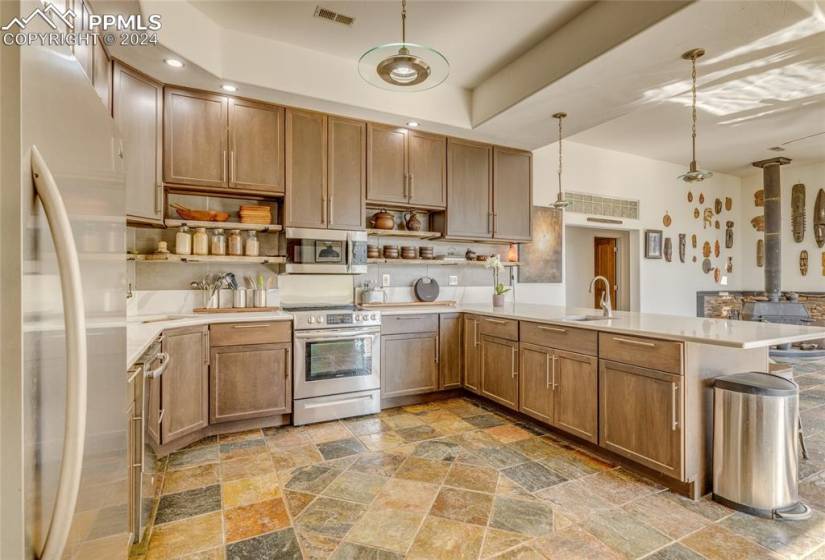Kitchen with decorative light fixtures, kitchen peninsula, appliances with stainless steel finishes, a raised ceiling, and sink