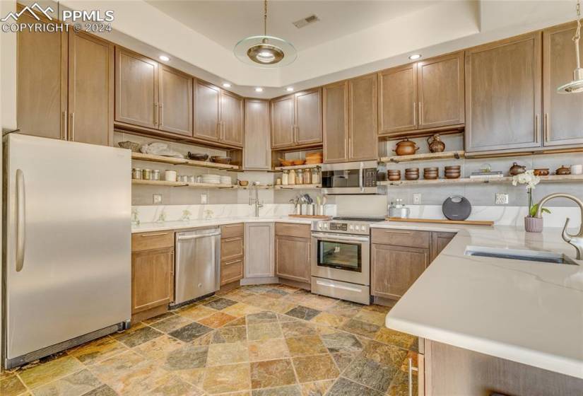 Kitchen with pendant lighting, appliances with stainless steel finishes, tile flooring, a raised ceiling, and sink
