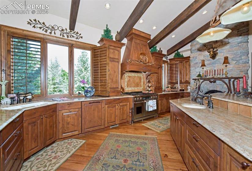 Kitchen with light wood-type flooring, light stone counters, range with two ovens, custom range hood, and sink