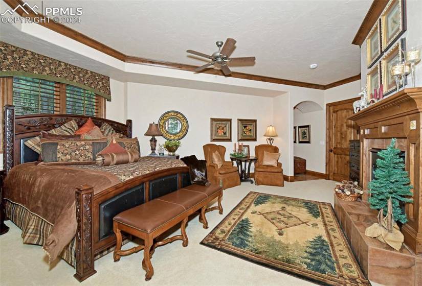 Carpeted bedroom with a tiled fireplace, ceiling fan, and crown molding