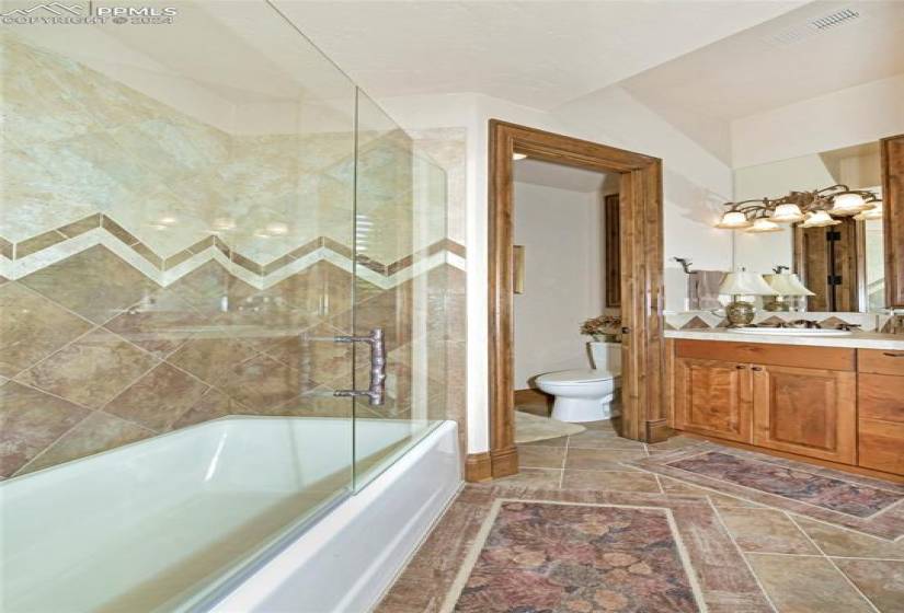 Full bathroom with toilet, tile flooring, vanity with extensive cabinet space, and bath / shower combo with glass door