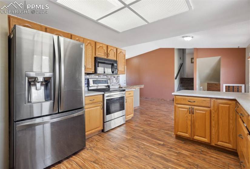 Kitchen with vaulted ceiling, appliances with stainless steel finishes, backsplash, and hardwood / wood-style flooring