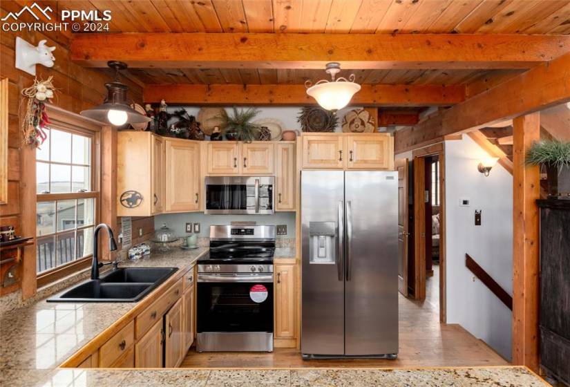 Kitchen featuring stainless steel appliances, beam ceiling, hanging light fixtures, light wood-type flooring, and sink