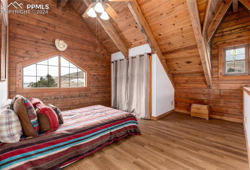 Bedroom featuring lofted ceiling with beams, wood ceiling, wood walls, and light hardwood / wood-style flooring