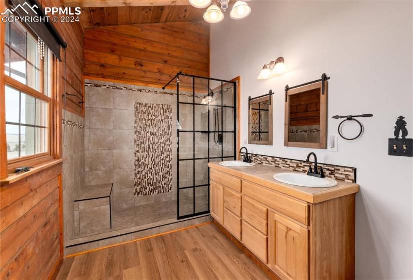 Bathroom with hardwood / wood-style flooring, an enclosed shower, dual sinks, oversized vanity, and lofted ceiling