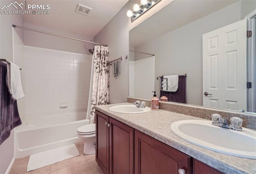Full bathroom featuring toilet, dual bowl vanity, vinyl flooring, and shower / bath combination with curtain