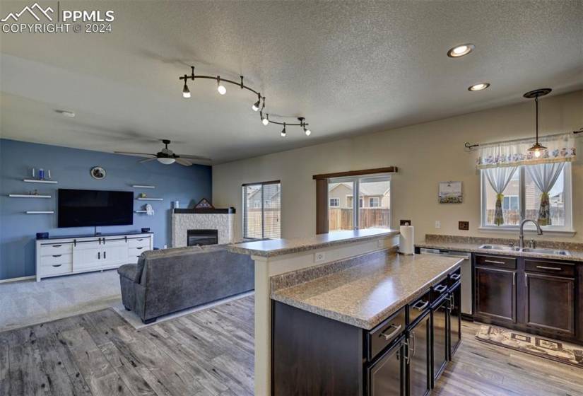 Kitchen featuring decorative light fixtures, ceiling fan, light carpet, dark brown cabinetry, and sink