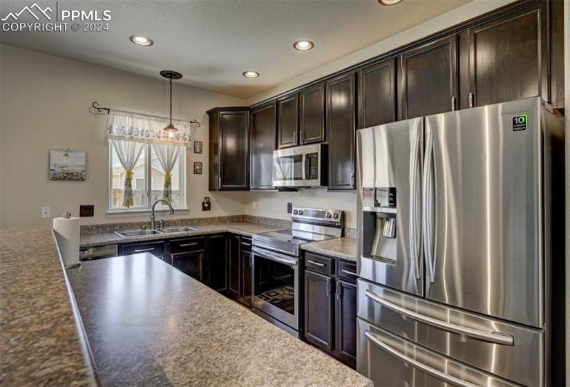 Kitchen featuring sink, dark stone counters, hanging light fixtures, stainless steel appliances, and dark brown cabinetry