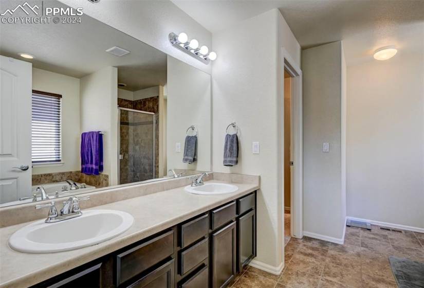 Bathroom with tile floors, dual sinks, vanity with extensive cabinet space, and independent shower and bath