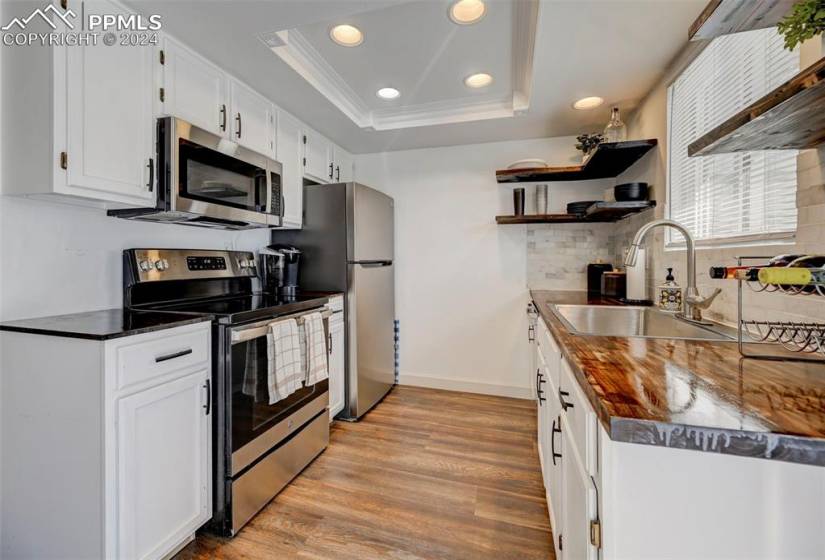 Kitchen with sink, a raised ceiling, white cabinets, appliances with stainless steel finishes, and light wood-type flooring