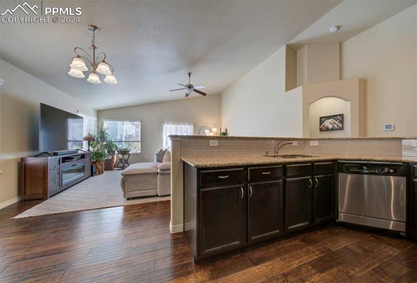 Kitchen with ceiling fan with notable chandelier, light stone counters, stainless steel dishwasher, vaulted ceiling, and dark hardwood / wood-style flooring