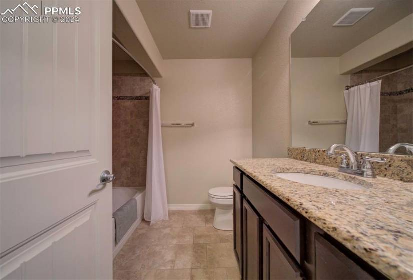 Full bathroom in basement featuring tile floors, large vanity, toilet, and shower / bathtub combination with curtain
