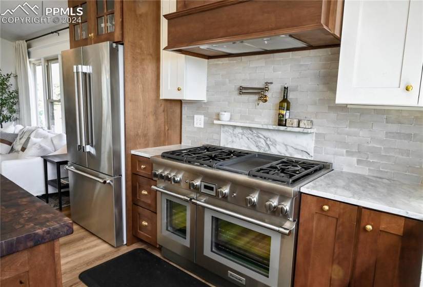 Kitchen with white cabinets, light hardwood / wood-style flooring, high end appliances, and tasteful backsplash