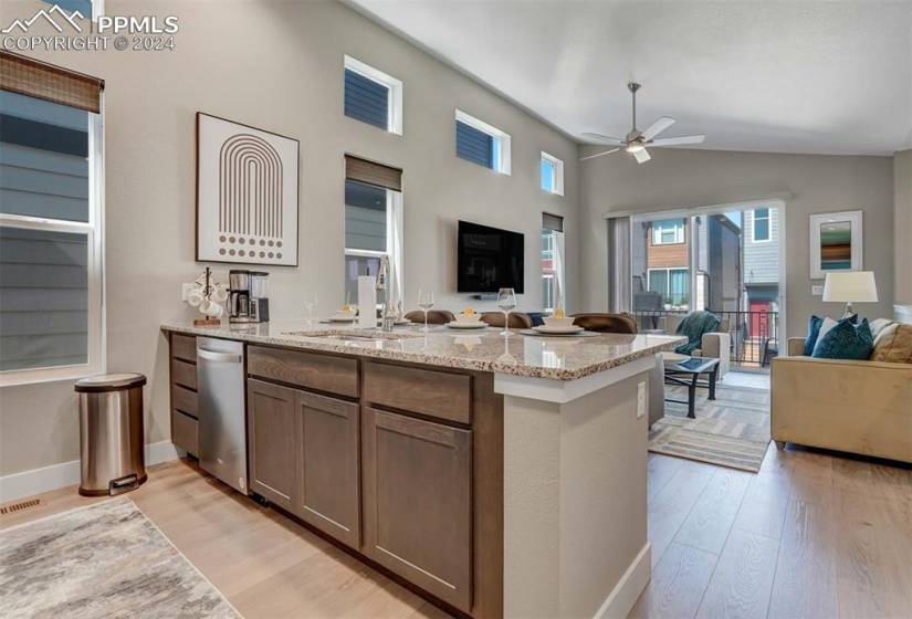 Kitchen featuring sink, dishwasher, light hardwood / wood-style floors, vaulted ceiling, and light stone countertops