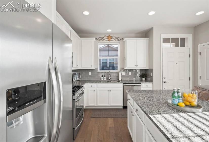 Kitchen featuring appliances with stainless steel finishes, white cabinets, backsplash, wood-style floors, and  stone counters