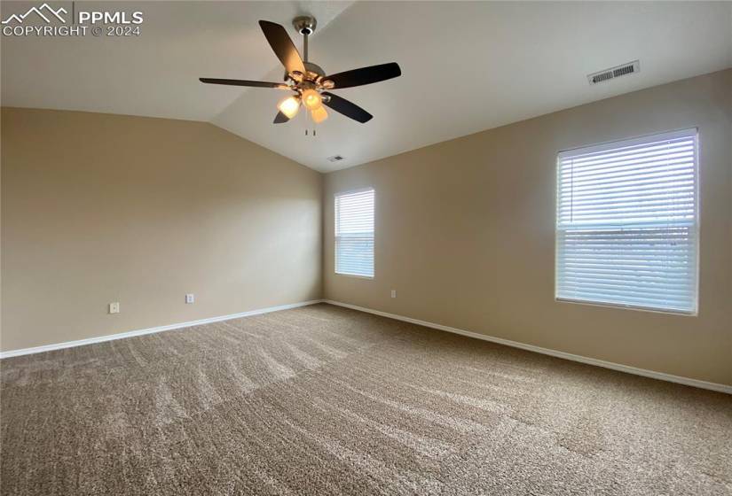 Carpeted primary room with vaulted ceiling and ceiling fan