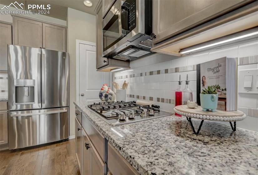 Kitchen with dark hardwood / wood-style floors, tasteful backsplash, appliances with stainless steel finishes, and light stone counters