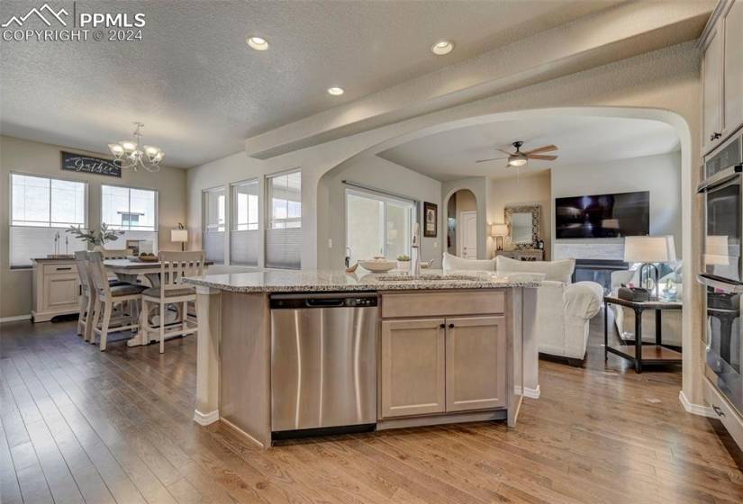Kitchen with light stone countertops, ceiling fan with notable chandelier, a fireplace, light hardwood / wood-style floors, and dishwasher
