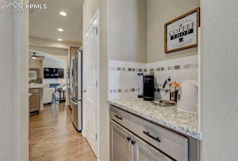 Kitchen featuring ceiling fan, tasteful backsplash, light hardwood / wood-style flooring, stainless steel refrigerator, and light stone counters