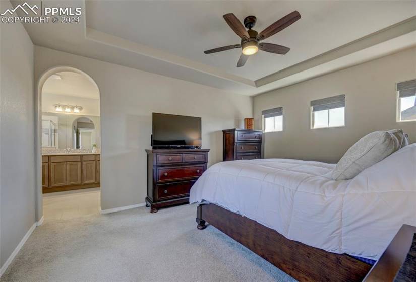 Bedroom with connected bathroom, light tile floors, ceiling fan, a tray ceiling, and sink