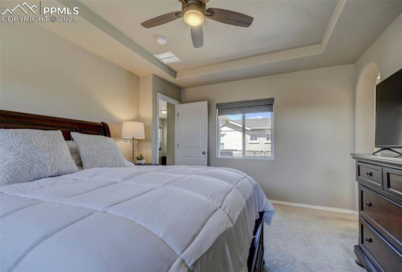 Bedroom with light colored carpet, ceiling fan, and a tray ceiling