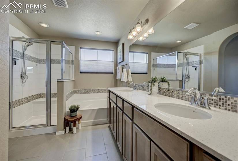 Bathroom featuring double sink, tile floors, shower with separate bathtub, vanity with extensive cabinet space, and tasteful backsplash