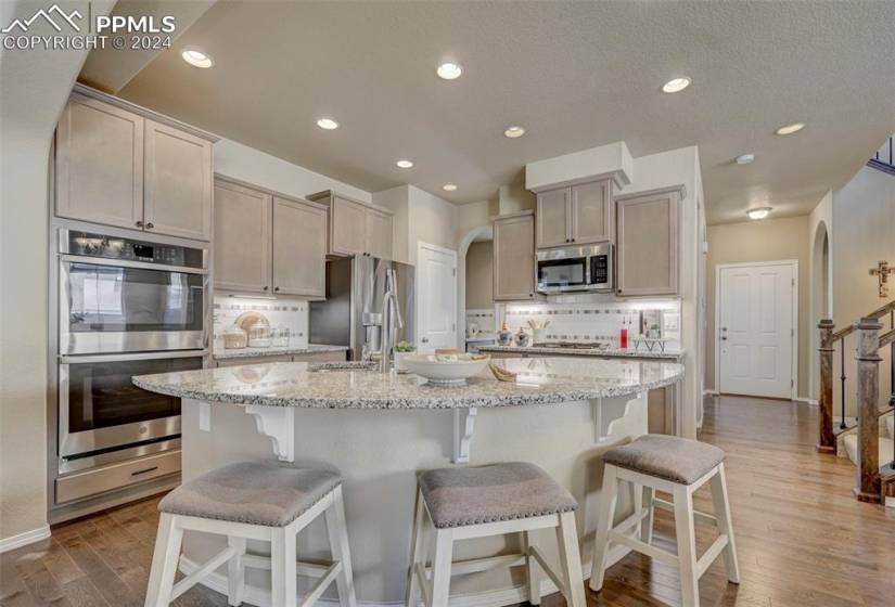Kitchen with light stone countertops, appliances with stainless steel finishes, light wood-type flooring, a center island with sink, and a breakfast bar area