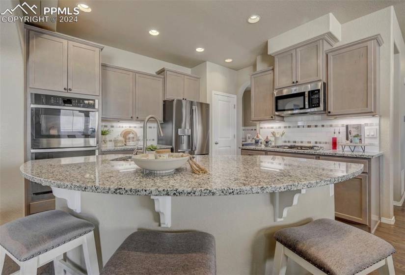 Kitchen with an island with sink, appliances with stainless steel finishes, wood-type flooring, tasteful backsplash, and a kitchen bar