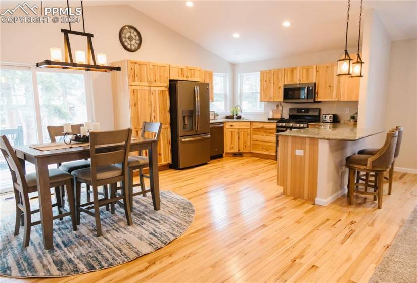 Kitchen with appliances with stainless steel finishes, light hardwood / wood-style flooring, light stone countertops, decorative light fixtures, and a notable chandelier