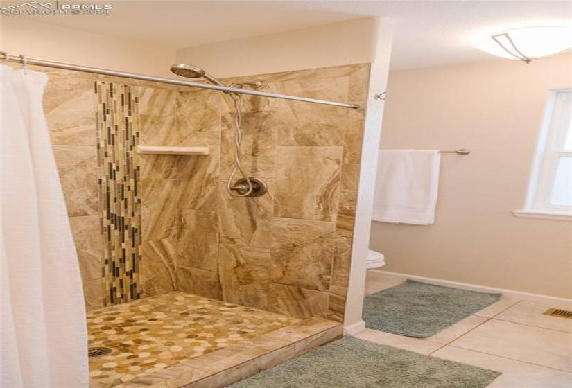 Bathroom with tile floors, toilet, and curtained shower