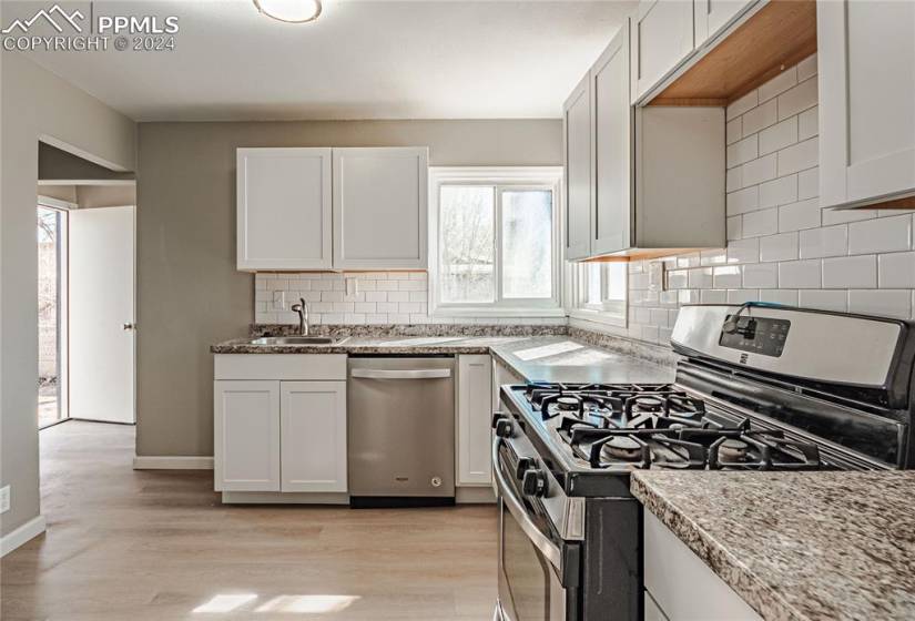Kitchen featuring tasteful backsplash, white cabinets, appliances with stainless steel finishes, and light wood-type flooring