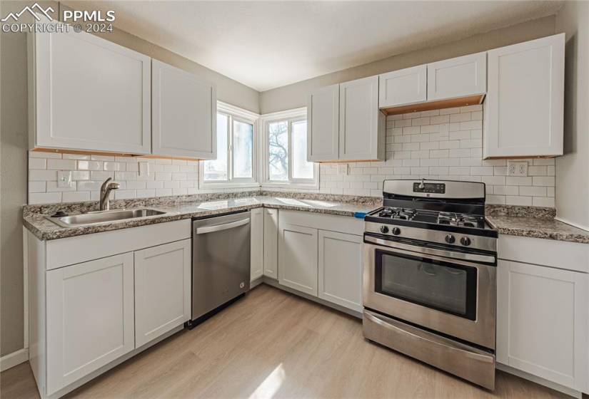 Kitchen with white cabinetry, appliances with stainless steel finishes, light wood-type flooring, and sink