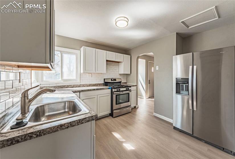 Kitchen featuring tasteful backsplash, stainless steel appliances, sink, white cabinetry, and light hardwood / wood-style flooring
