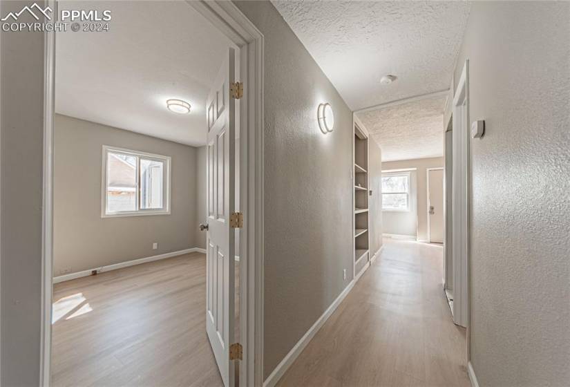 Corridor featuring built in features, a textured ceiling, a wealth of natural light, and light hardwood / wood-style flooring