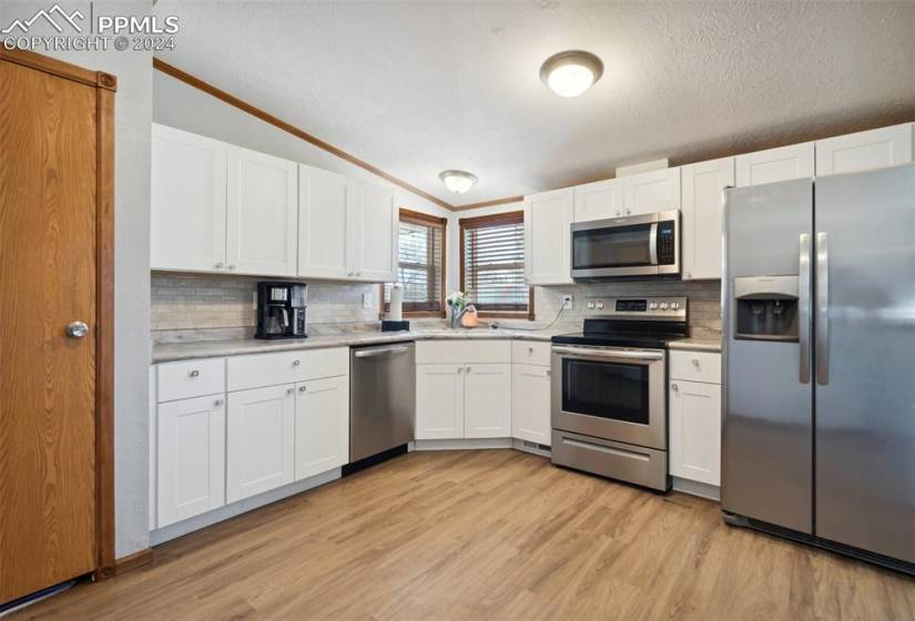 Modern style kitchen w/ white cabinets, SS appliances, eat-in area, pantry, and LVP flooring