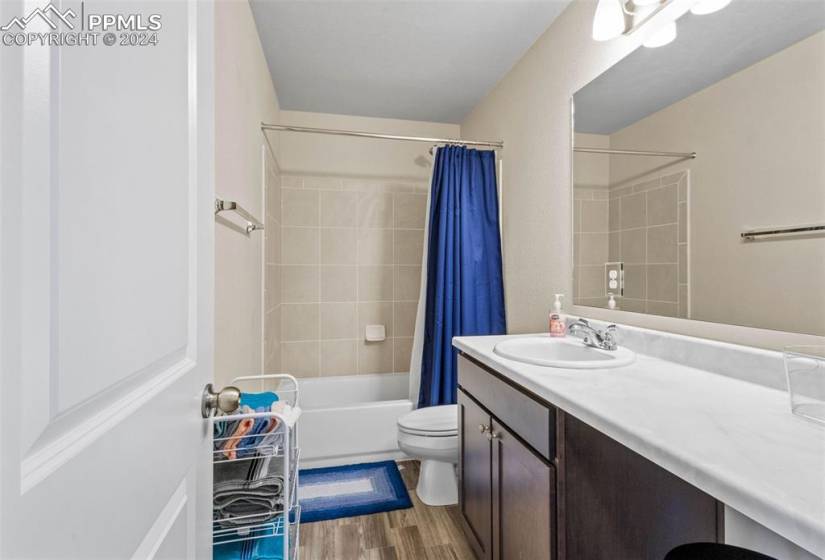 Full bathroom with oversized vanity, toilet, shower / tub combo with curtain, and hardwood / wood-style flooring