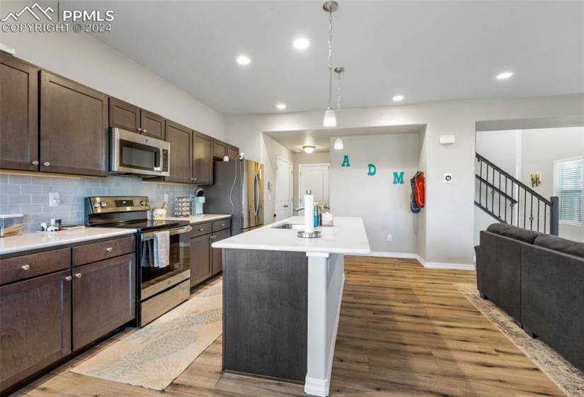 Kitchen featuring hanging light fixtures, appliances with stainless steel finishes, light hardwood / wood-style floors, tasteful backsplash, and dark brown cabinetry