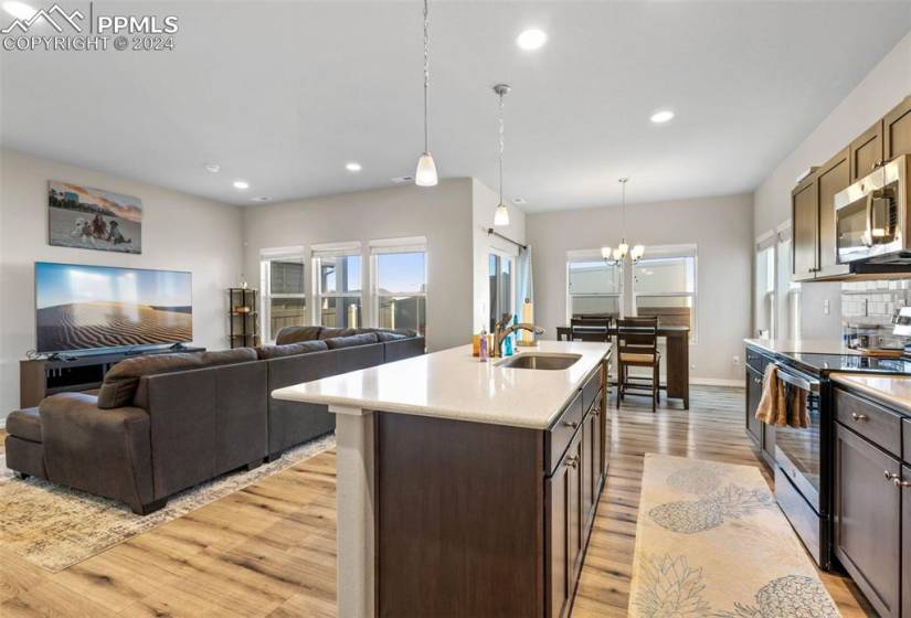 Kitchen with appliances with stainless steel finishes, hanging light fixtures, a notable chandelier, sink, and light hardwood / wood-style flooring