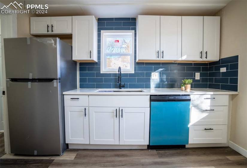 Kitchen with stainless steel refrigerator, tasteful backsplash, wood-type flooring, white cabinetry, and dishwashing machine