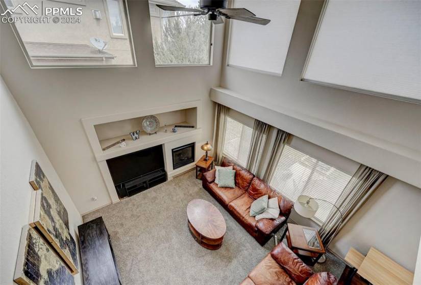Carpeted living room with ceiling fan, built in features, and a towering ceiling