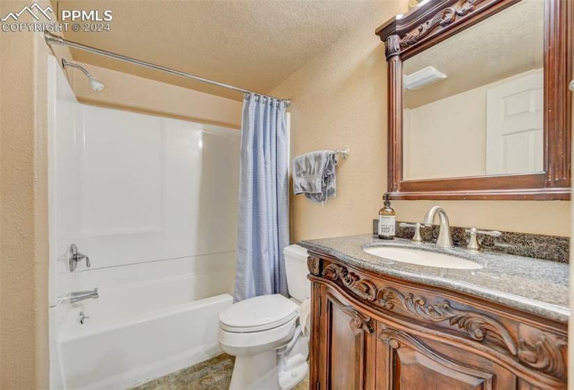 Basement Full bathroom featuring tile flooring, a textured ceiling, toilet, vanity, and shower / tub combo